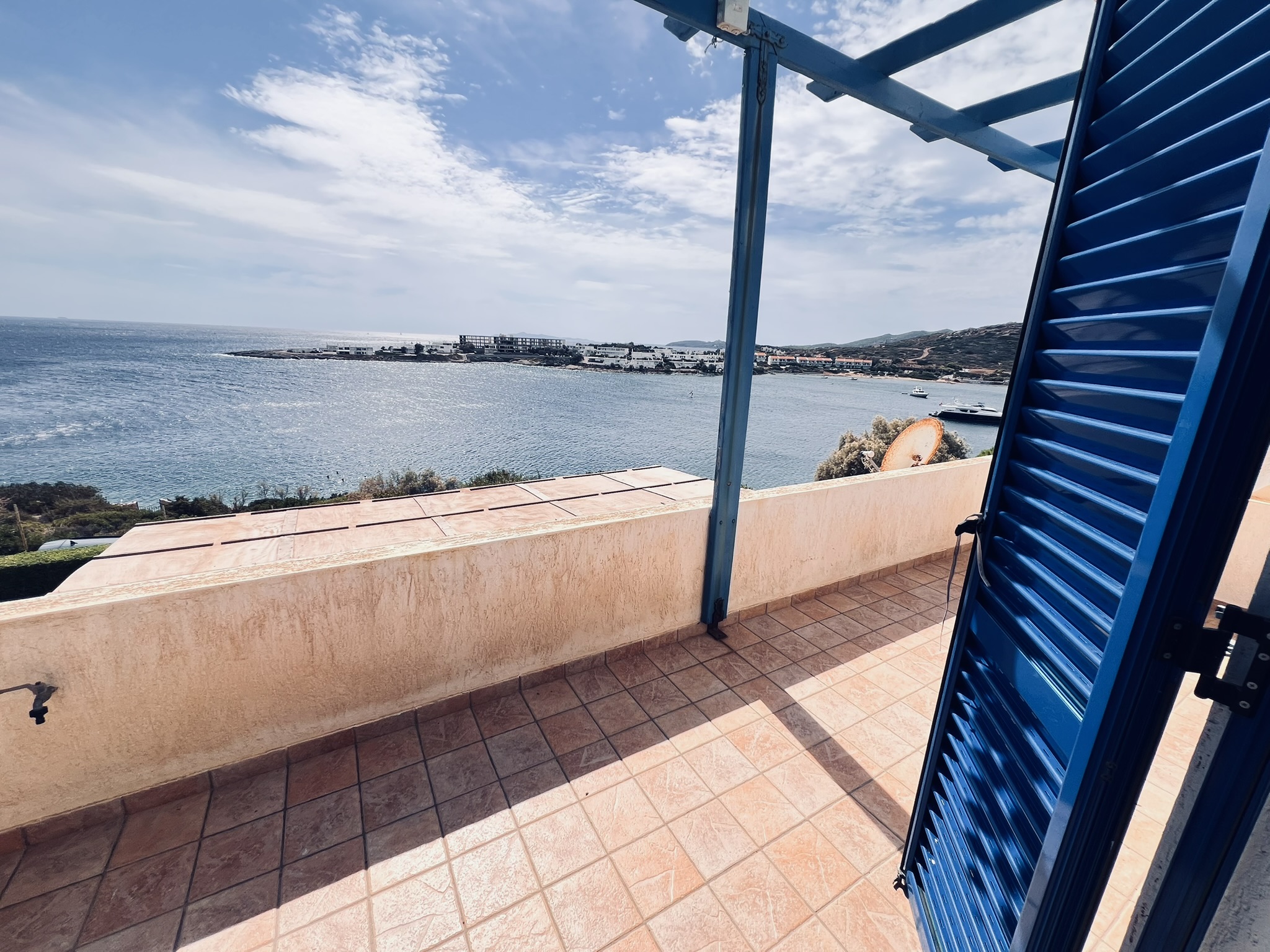 The view from the master bedroom's sea-facing balcony — the bay, sailboats, and the blue shutter
