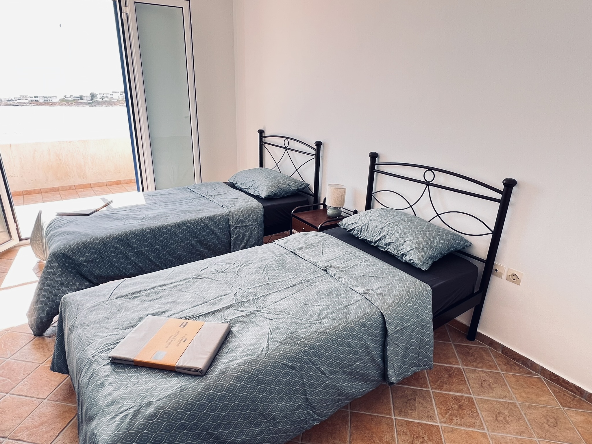 The second bedroom — two single beds by the open balcony door, with the sea view beyond